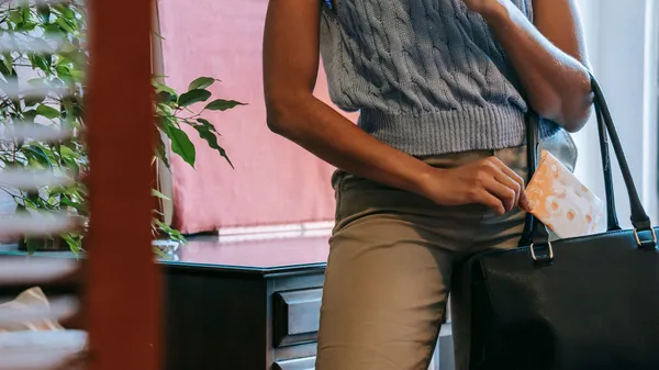 Crop unrecognizable African American female in casual clothes putting sanitary towel in black leather bag