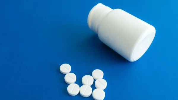 White tablets spilling from a plastic container on a solid blue background.