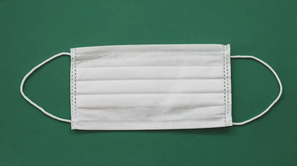 White surgical mask placed against a vibrant green background for health safety themes.
