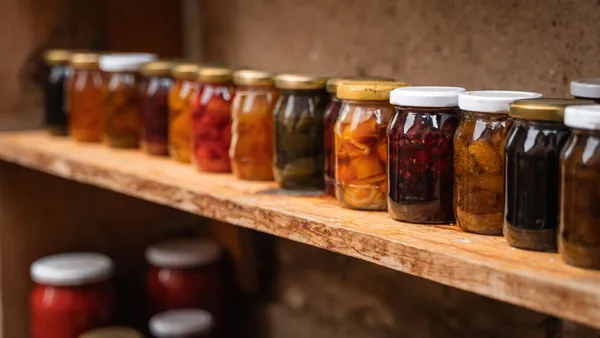 Homemade preserves in mason jars neatly arranged on a rustic wooden shelf.
