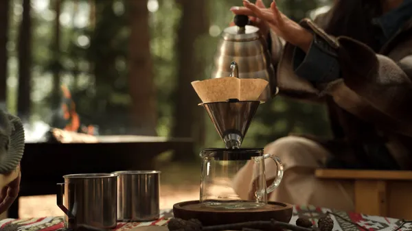 A serene outdoor scene capturing a hand brewing coffee with a pour over method, highlighting nature and simplicity.
