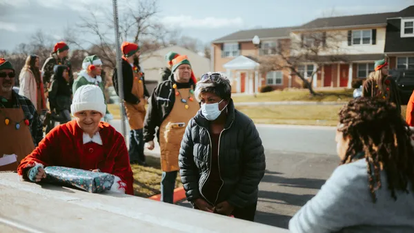 A neighborhood holiday gathering featuring adults dressed in elf costumes distributing gifts on a street.