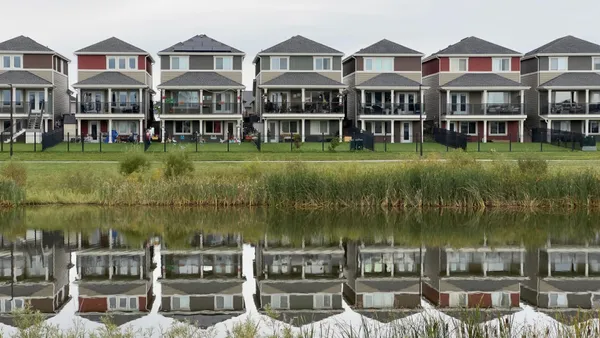 A row of modern houses reflected in a calm pond, showcasing serene suburban architecture.