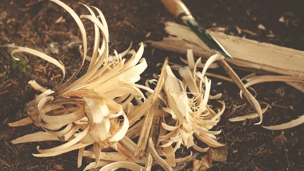 Woodworking knife and wood shavings on ground, showcasing craftsmanship in a rustic outdoor environment.