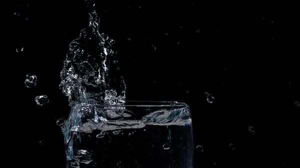Close-up of water splashing in a glass against a black background.