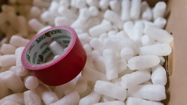 Close-up of red duct tape on packing peanuts in a cardboard box for shipping or moving.