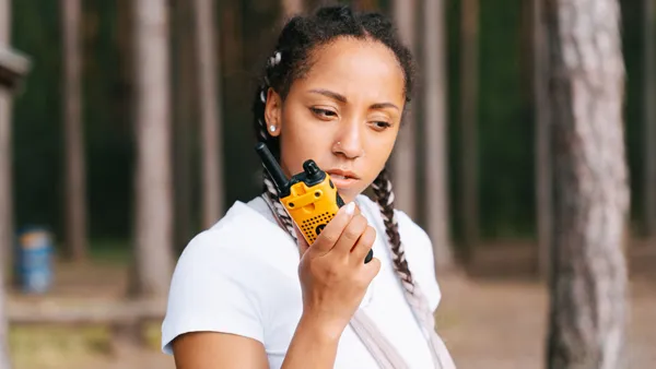 Focused young woman communicates using a two-way radio in an outdoor forest setting.