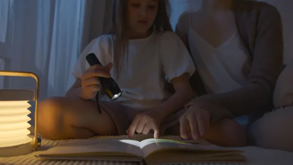 A child and adult reading a book at night using a flashlight, creating a cozy atmosphere.