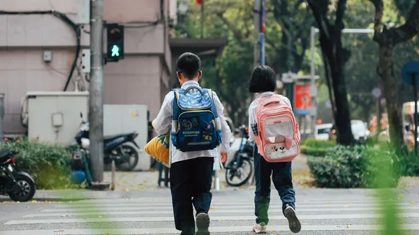 Two children with backpacks crossing a street at a pedestrian crossing.