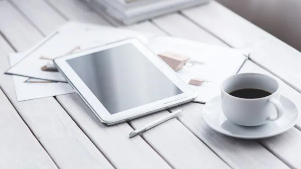 White tablet with stylus and coffee cup on modern office desk setup.
