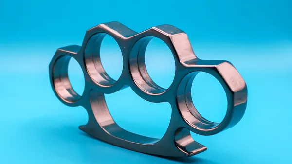 Close-up of steel brass knuckles against a vibrant blue backdrop, studio shot.