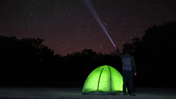 A lone camper observes the starlit sky near a glowing tent in Aksaray, Türkiye.