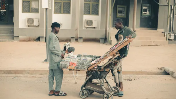 Urban street scene showing a vendor selling traditional goods to a customer.