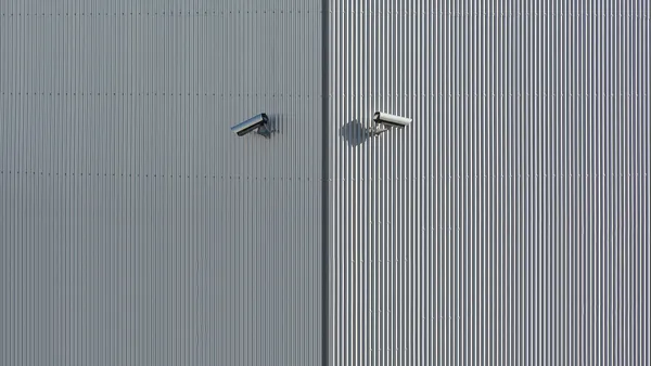 Corrugated metal wall with two mounted security cameras in a minimalist style.