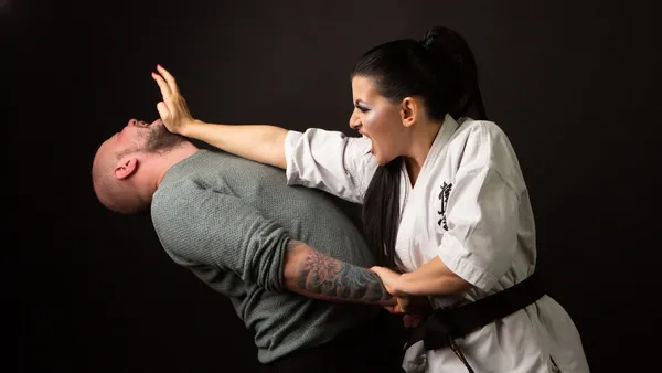 A woman in karate attire defends herself against a man in a martial arts demonstration.
