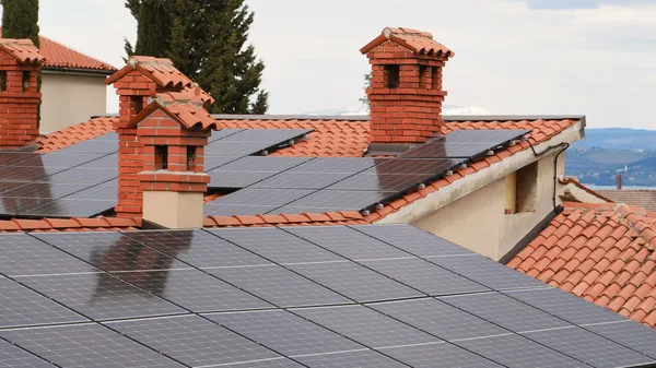 Solar panels on tiled roofs of houses with chimneys, capturing clean energy.