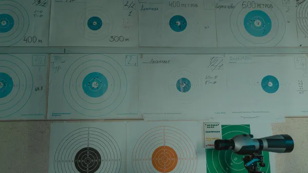 Image of a target shooting setup with a spotting scope and displayed target papers indoors.