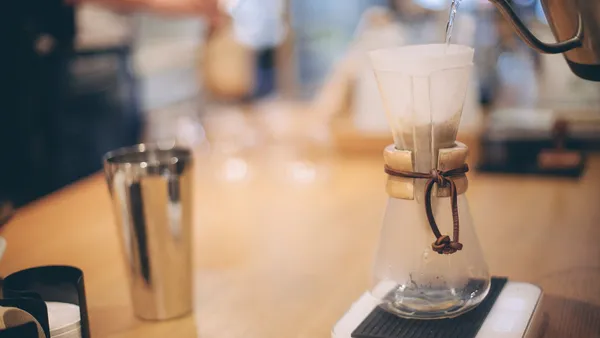 Barista making coffee using drip kettle pouring water into glass flask with paper filter with grounded coffee beans