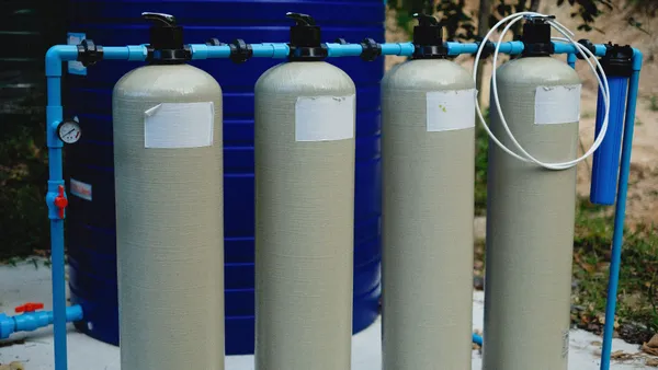 Four beige tanks in an outdoor water treatment setup with blue piping.
