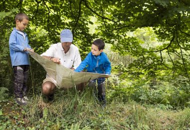 Father and children reading map in a wild green forest nature.
